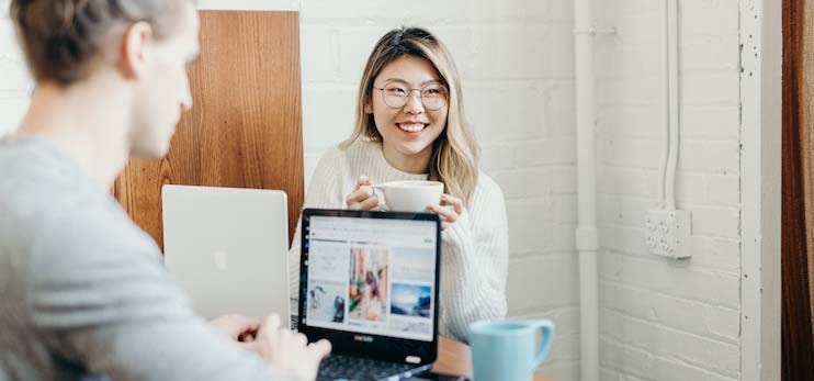 En leende ung kvinna i glasögon och mellanlångt blont hår, hon har en laptop framför sig