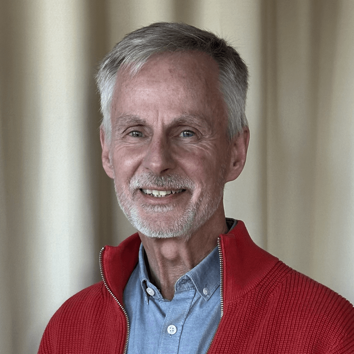 Man med grått hår, blå skjorta och röd tröja.