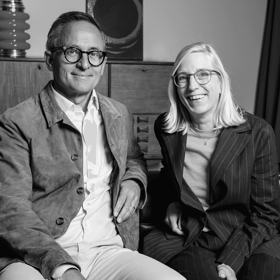 Blond kvinna och man med brunt hår sitter och poserar framför kameran.