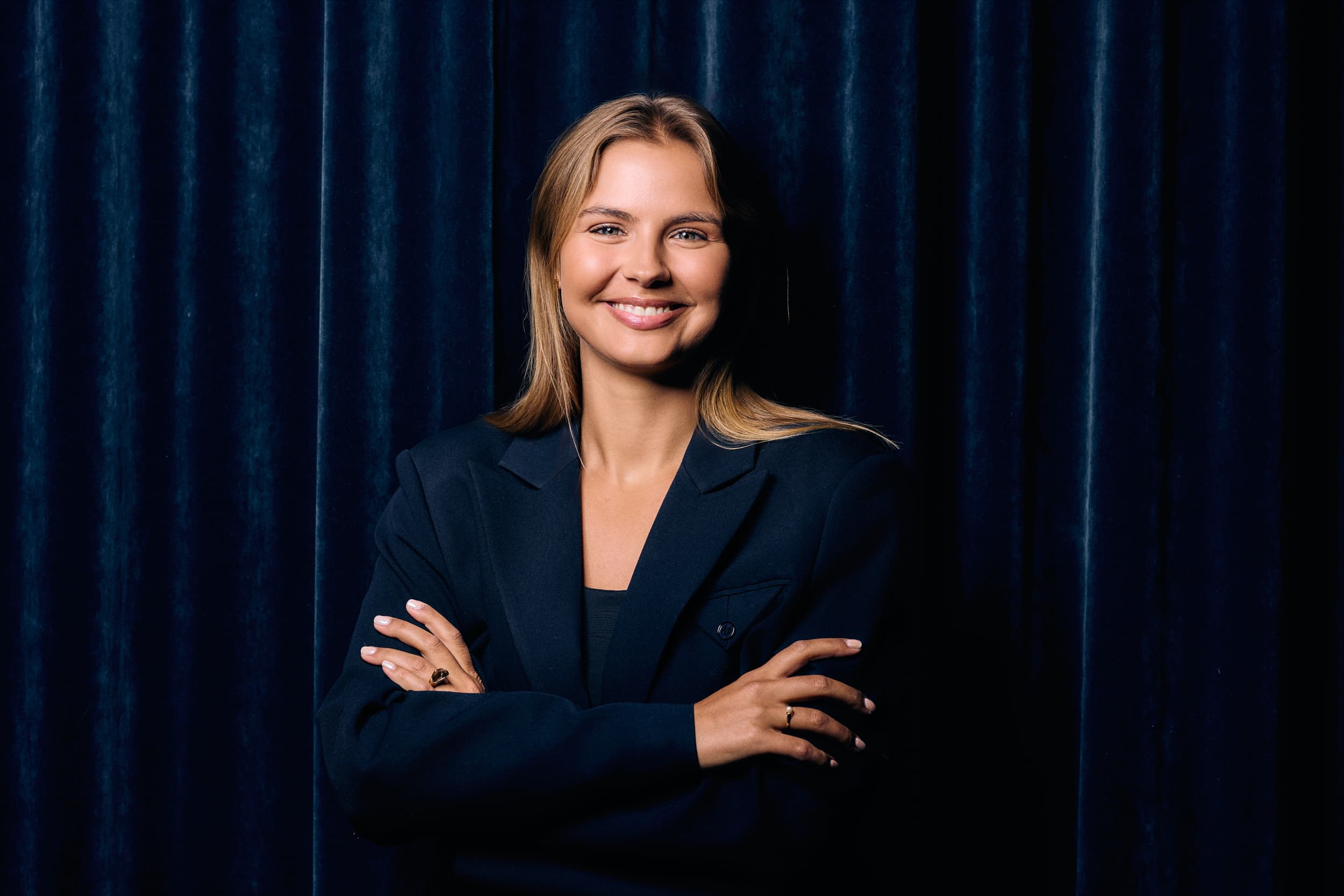 Kvinna med kavaj och brunt hår ler in i kameran