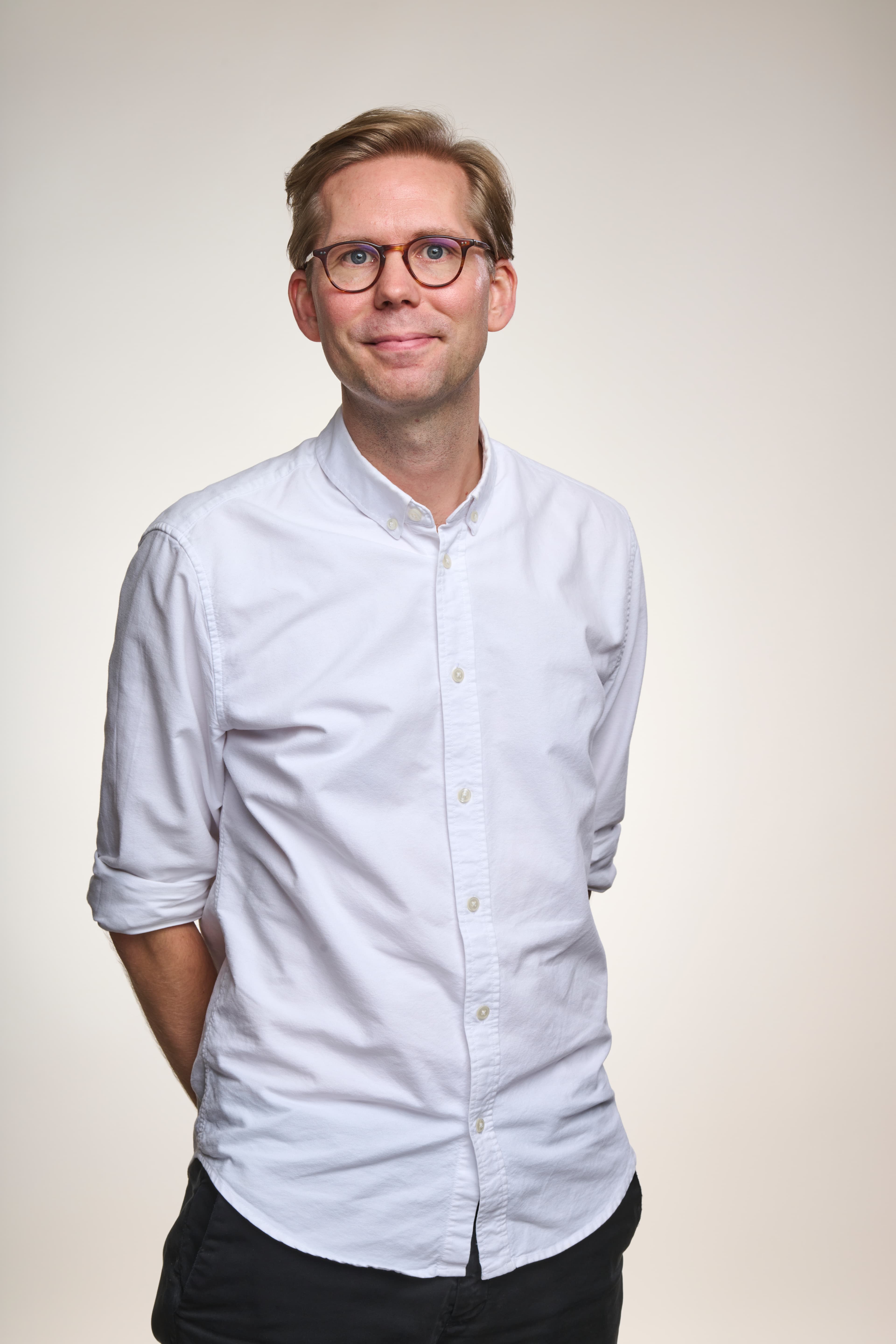 Blond man med vit skjorta och glasögon poserar för kameran.