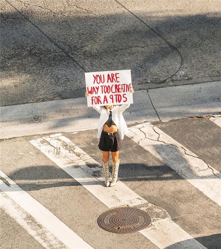 Kvinna som håller i en skylt med texten You are too creative for a 9 to 5