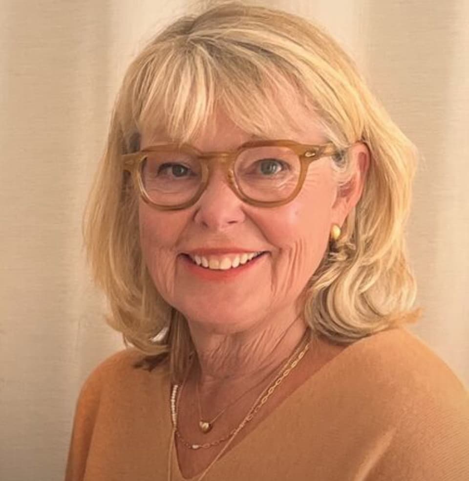 Blond kvinna med glasögon ler mot kameran.