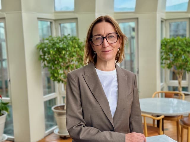 Kvinna med page, glasögon, vit t-shirt och beige kavaj.