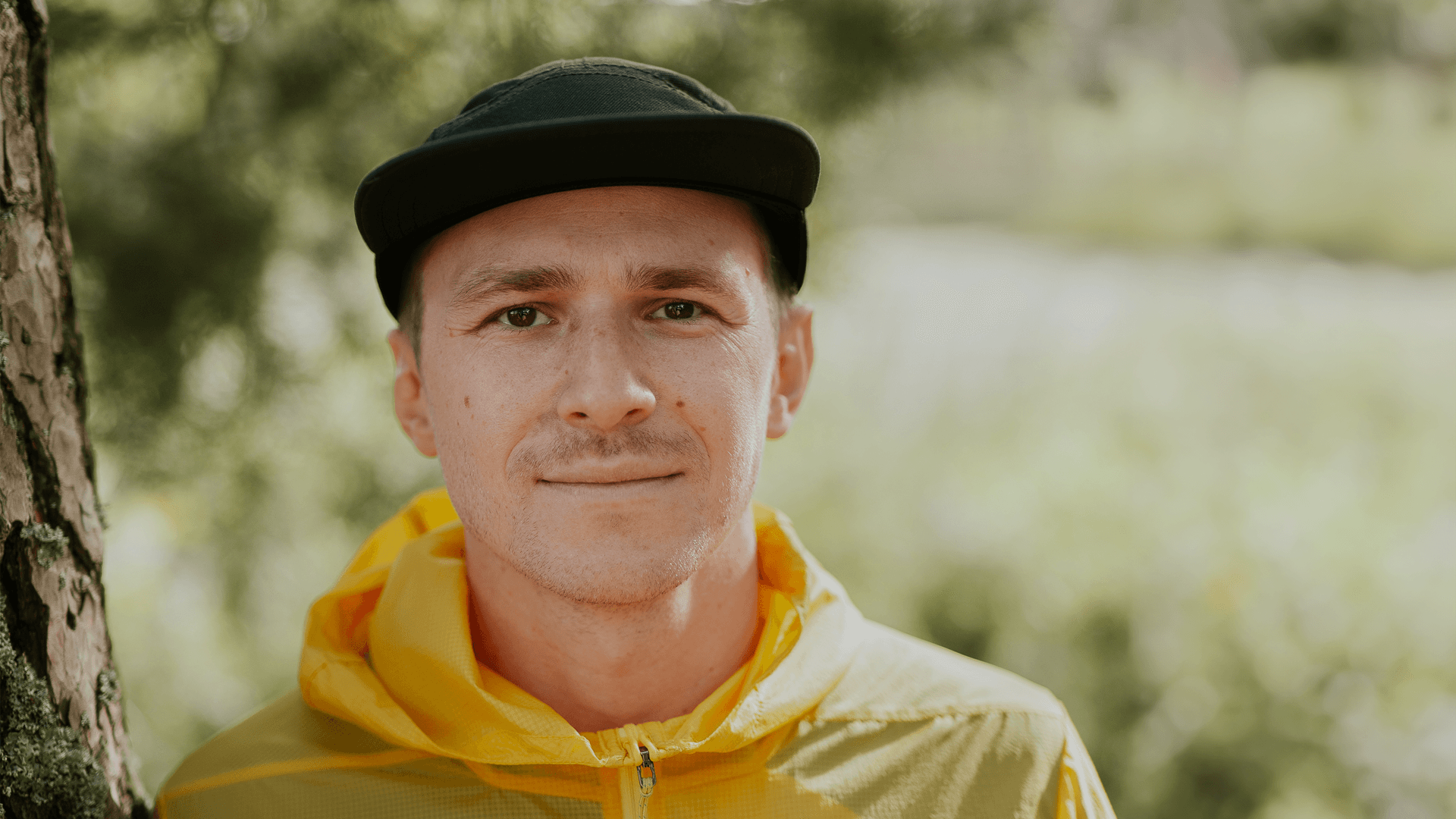 Porträtt av en man i svart keps och gul jacka ler mot kameran