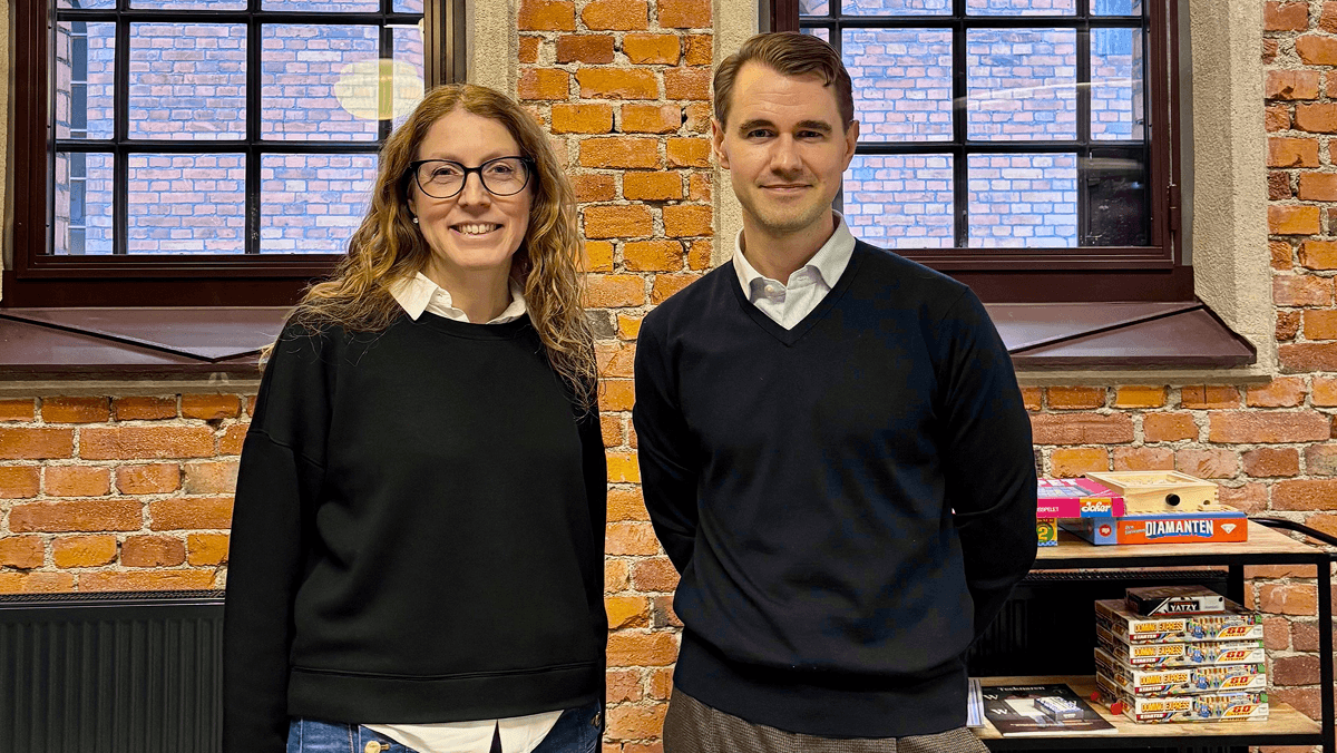 Bild på en kvinna och en man i rustik miljö. Båda ler och tittar in mot kameran.