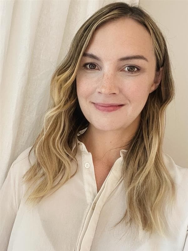 Blond kvinna med vit skjorta ler mot kameran för porträttbild.