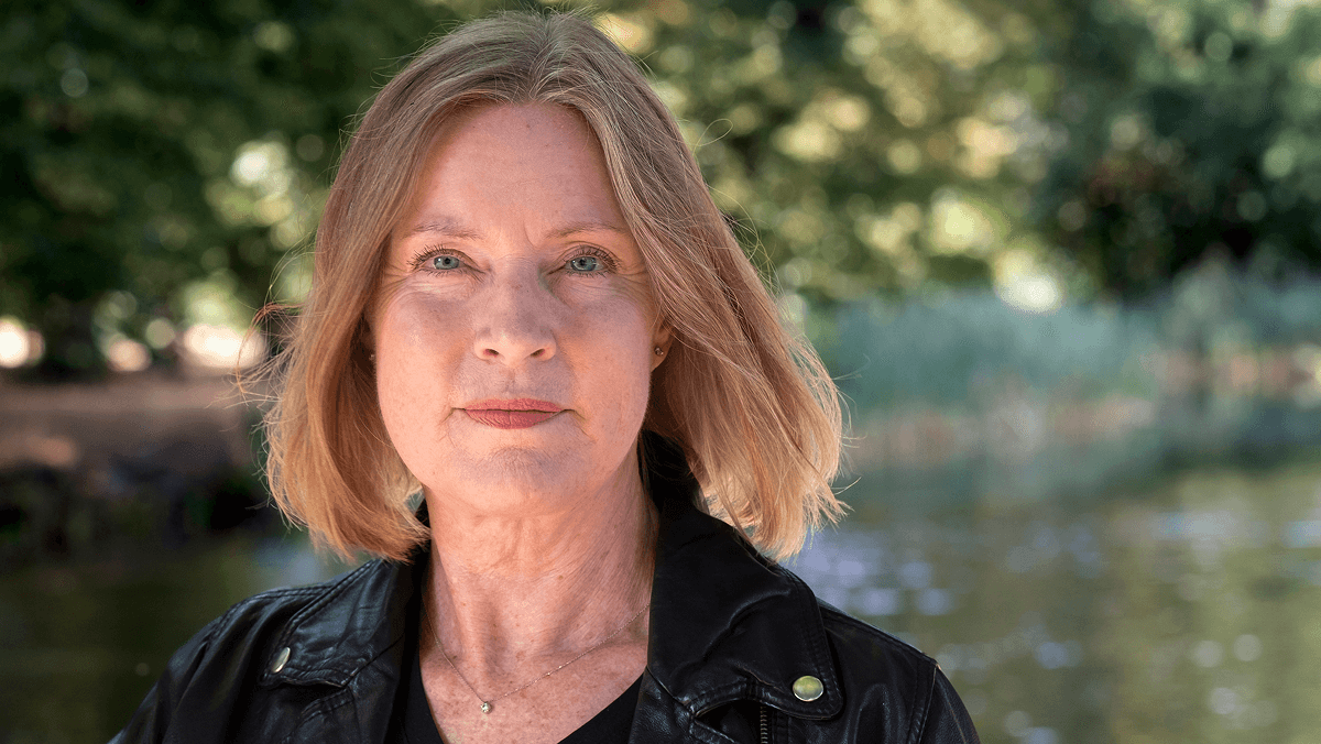 Blond kvinna med svart skinnjacka i naturbakgrund.
