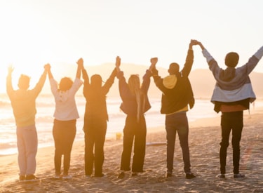 Sex personer står på en strand, håller varandra i händerna och sträcker upp händerna i luften