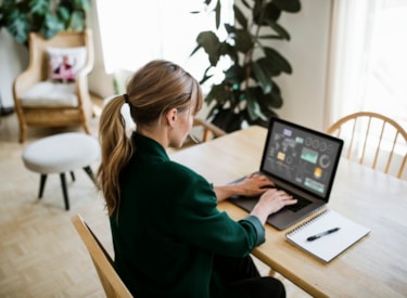 Vit kvinna med uppsatt hår sitter vid ett bord och jobbar vid en dator