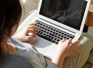 En kvinna som sitter med en dator i knät. 