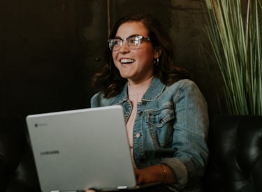 En kvinna med brunt hår som har en dator i knät och ler. 