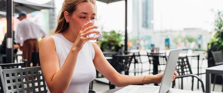 Kvinna dricker kaffe framför skärm