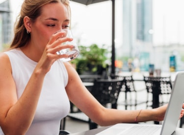 Kvinna dricker kaffe framför skärm