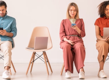 En man och två kvinnor sitter på stolar och läser i skärmar