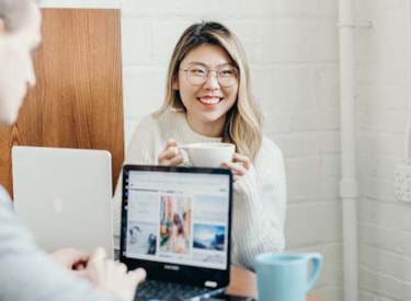 En leende ung kvinna i glasögon och mellanlångt blont hår, hon har en laptop framför sig