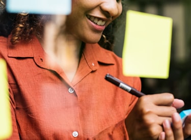 Vit kvinna i orange blus skriver med en penna på en post-it.