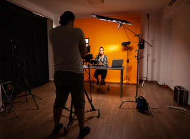 En stående person filmar en annan person som sitter framför en orange vägg