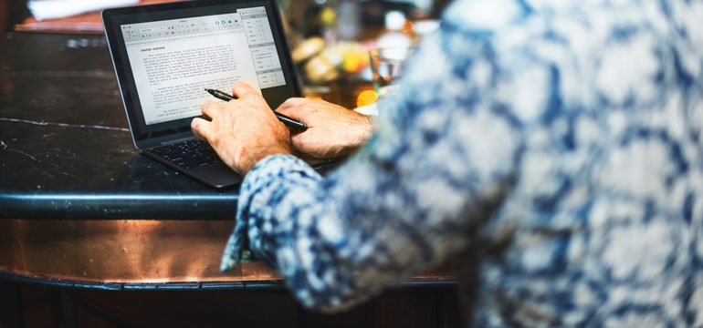 En person i blå skjorta sitter och arbetar vid sin dator